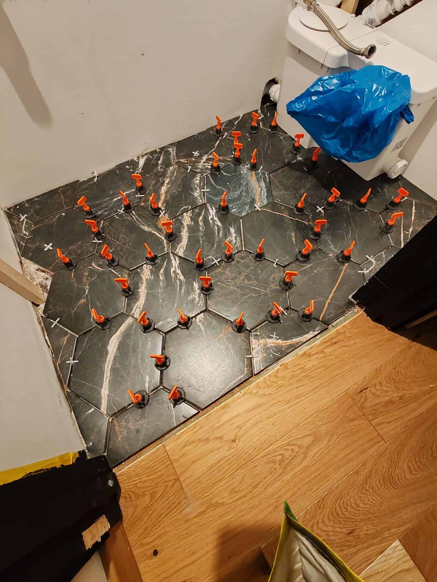 Hexagonal marble-effect floor tiles being installed in a bathroom with tile levelling clips in place