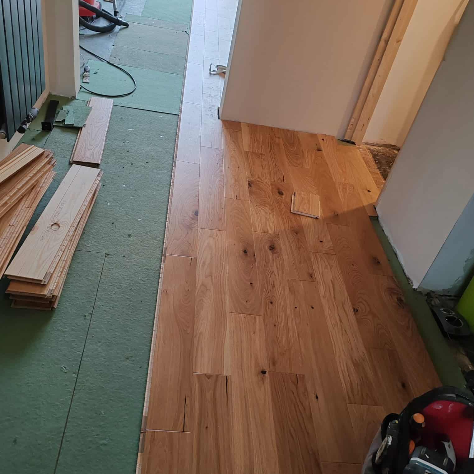 Solid oak flooring being installed in a hallway with underlay and flooring boards ready for fitting