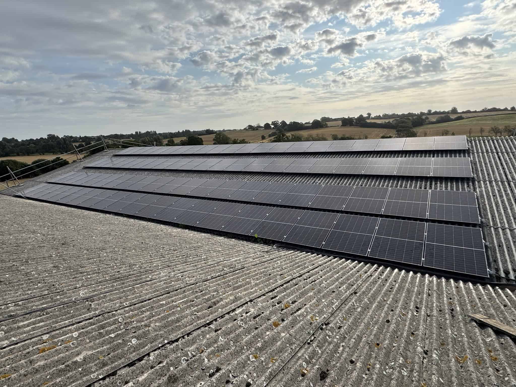 Solar panels installed across the roof of a rural agricultural building.