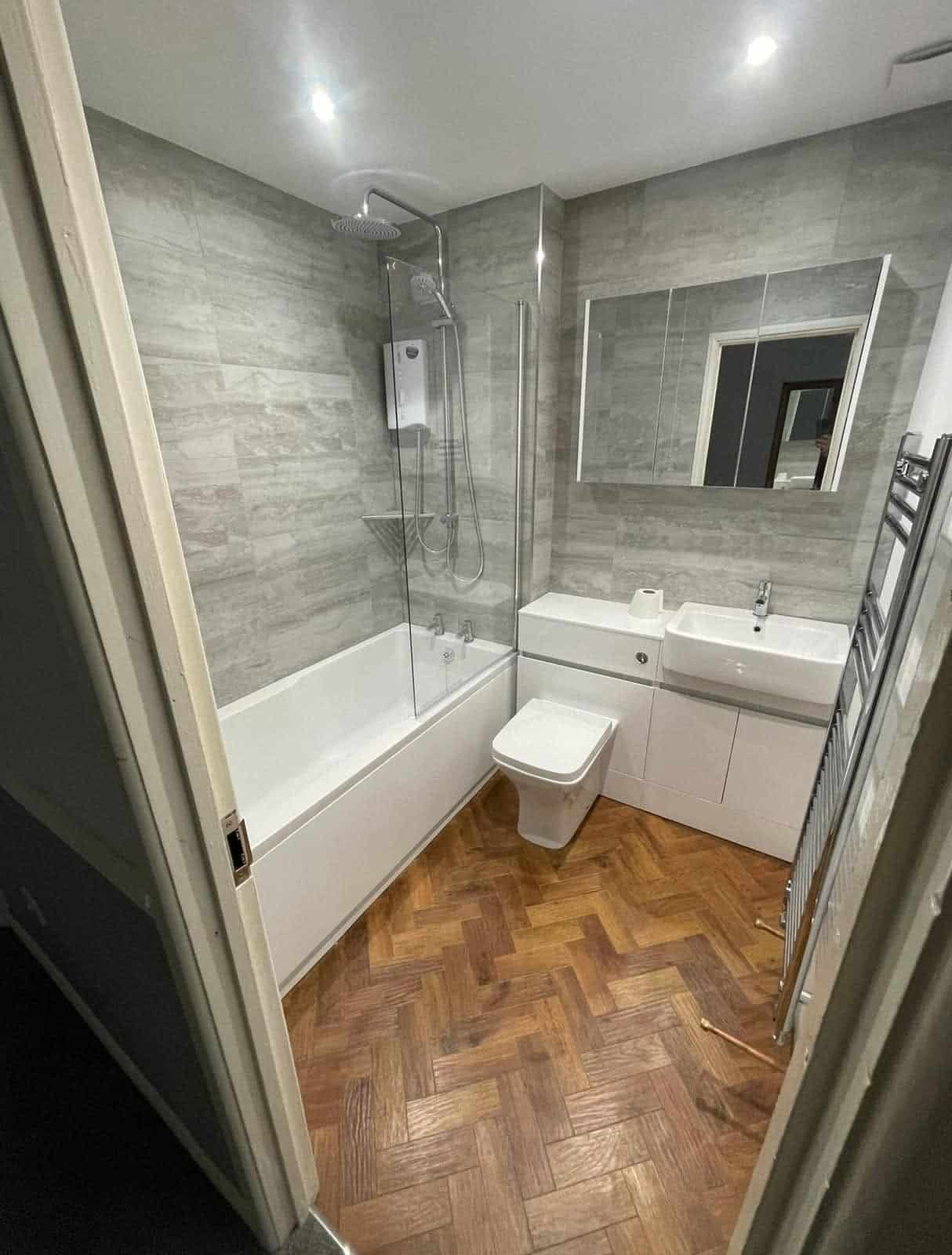 Modern bathroom with bath, overhead shower, wall-hung toilet, vanity unit and grey tiled walls