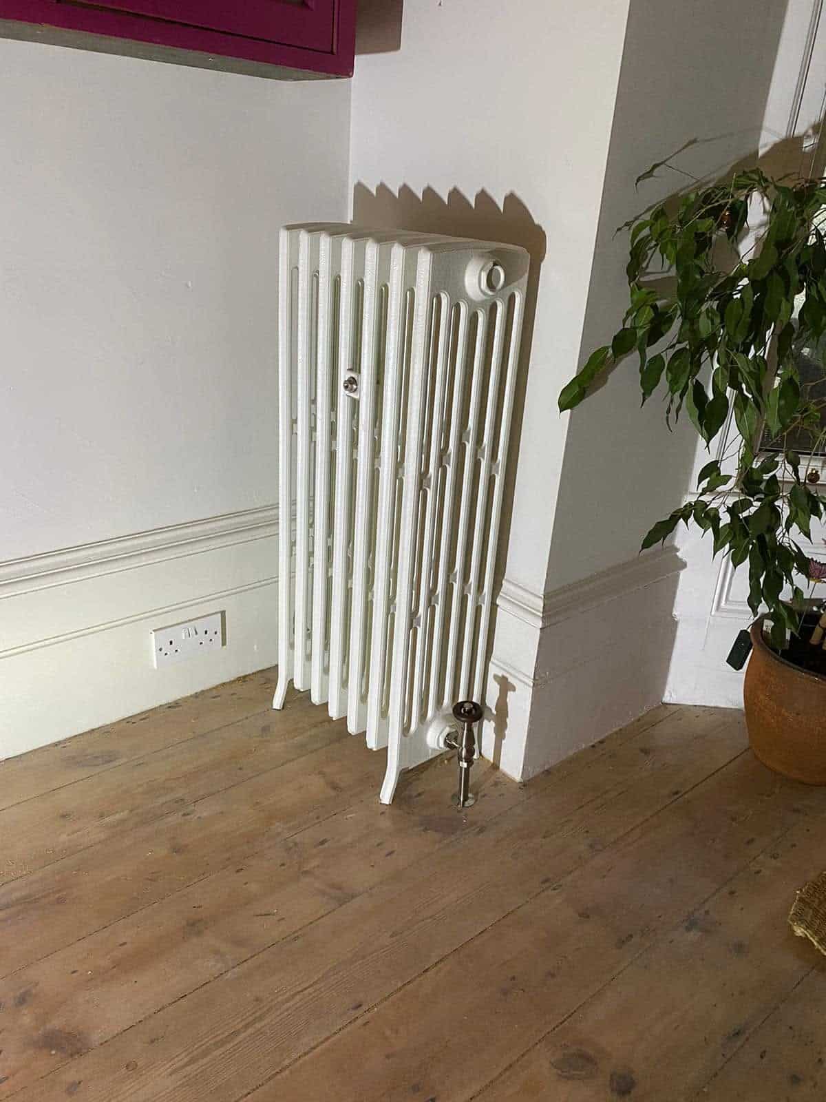 Traditional white column radiator installed against an interior wall with exposed valve fittings