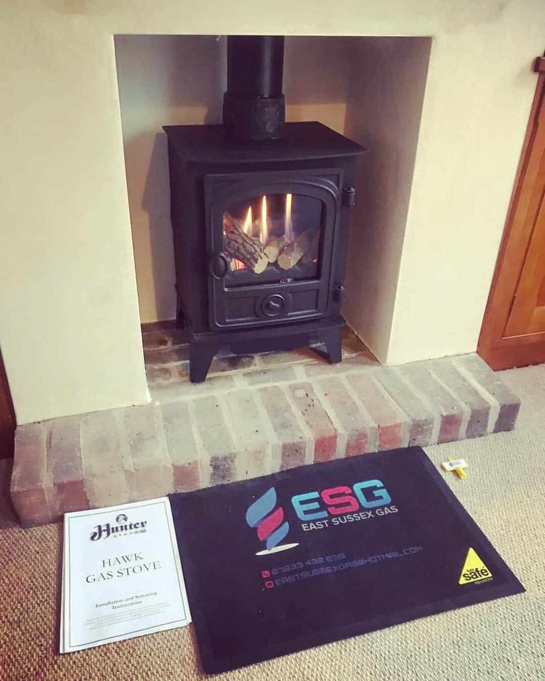 Black gas stove with visible flames installed within a recessed fireplace and brick hearth