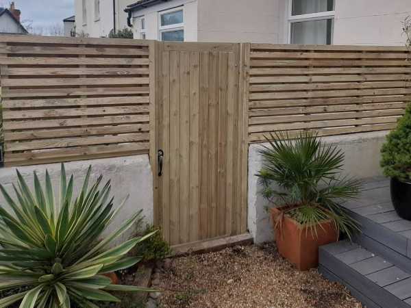 Timber garden gate with matching horizontal slatted fence panels surrounding a front garden in Bexhill