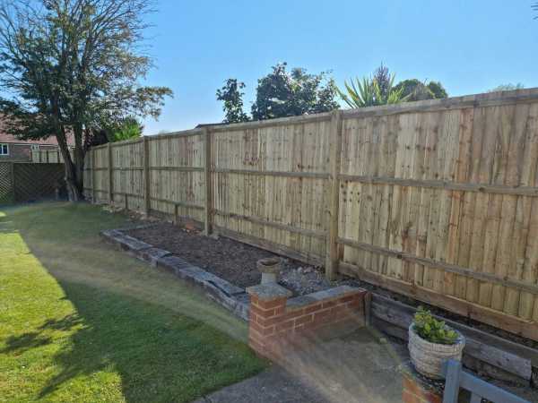 Long timber panel fence installed along a residential garden boundary with lawn and planting beds in Bexhill