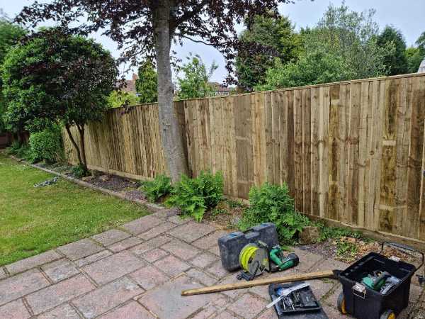 New timber panel garden fence installed alongside a paved patio and mature trees in Bexhill