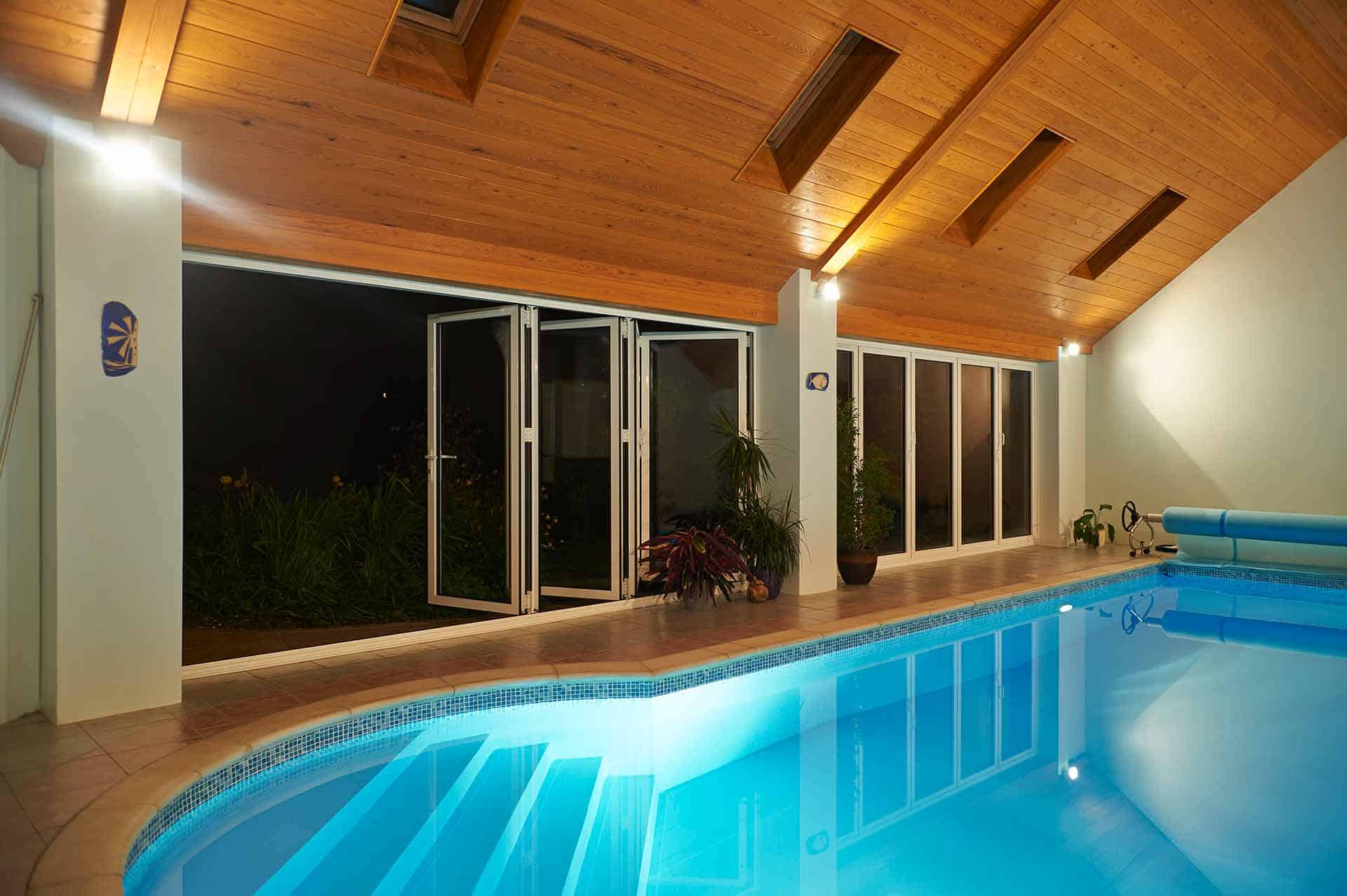 Large aluminium bifold glass doors opening onto a garden beside an indoor swimming pool