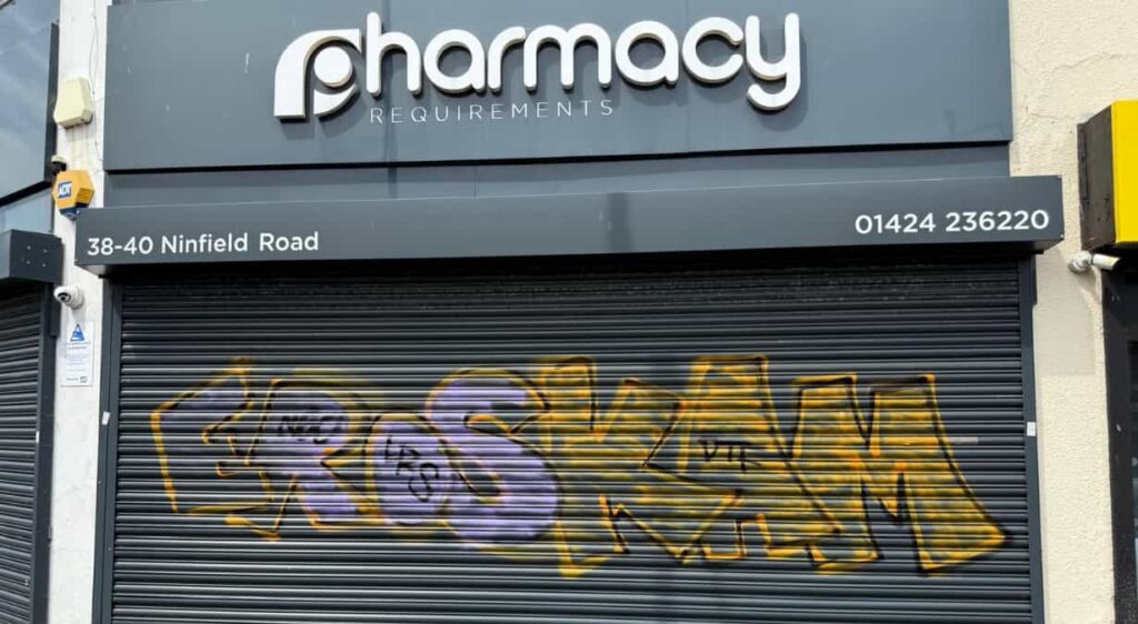 Graffiti sprayed across the metal security shutters of Pharmacy Requirements in Sidley following overnight vandalism.